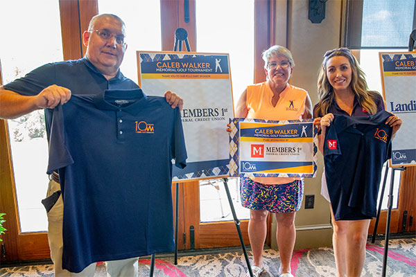 Representatives holding event polo shirts and sponsor signs at the Caleb Walker Memorial Golf Tournament.