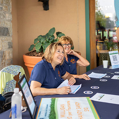 A Week Away volunteers wearing AWA polos at the golf tournament registration table.