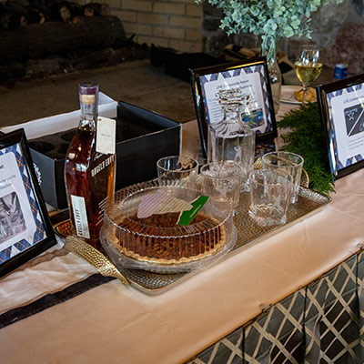 Bourbon and dessert auction prize package displayed on a table with framed item descriptions.