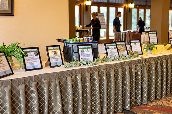 A row of silent auction items and donor signs displayed on a draped table at a charity golf event.