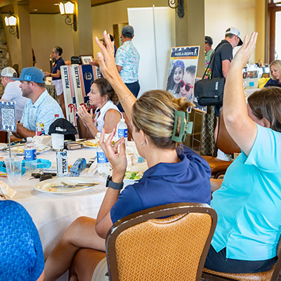 Attendees of the Caleb Walker Memorial Golf Tournament raising their hands and participating in the auction.