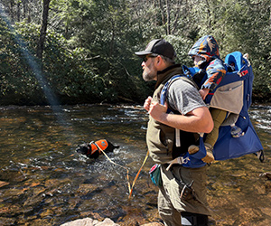 A man hiking by a creek with his dog.