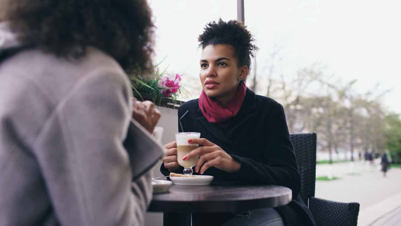 Two friends catch up over coffee at a wooden table.