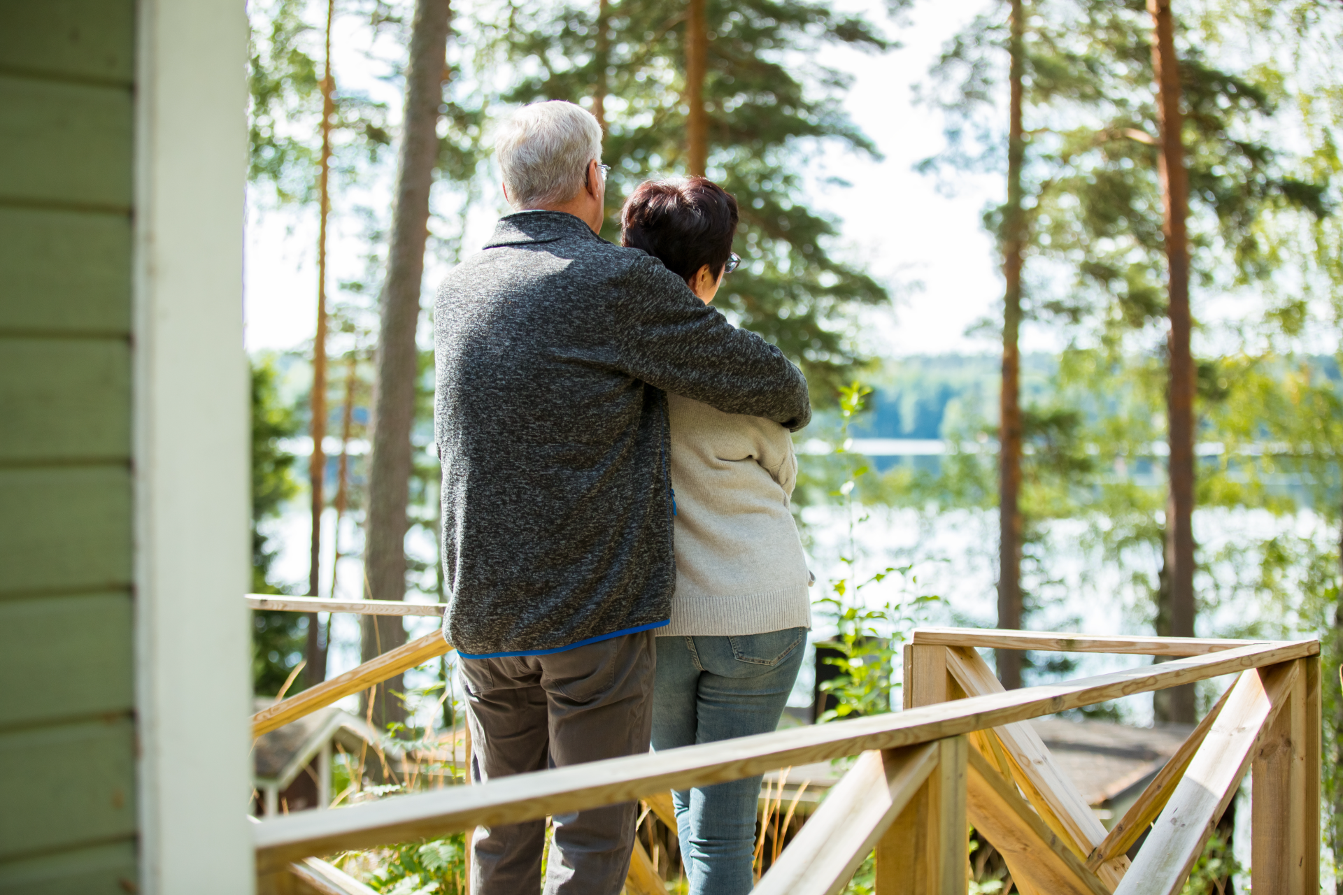 Two people hugging on a porch in the woods looking out over a lake.